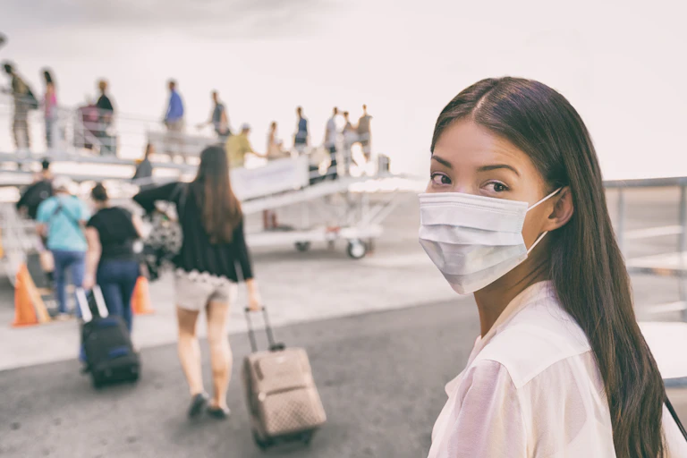 A woman in a face mask looks back as a line of people board a small plane ahead of her