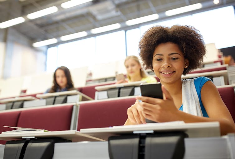 Une jeune fille consulte son téléphone cellulaire dans une salle de classe