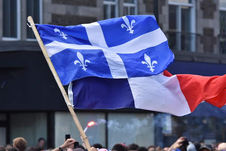 Un drapeau québécois et un drapeau français flottent au vent devant des édifices lors d'une manifestation