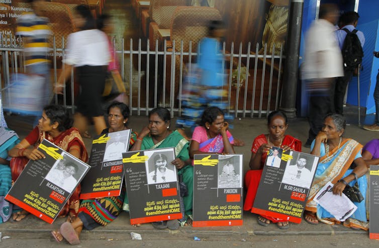 Women sit holding signs