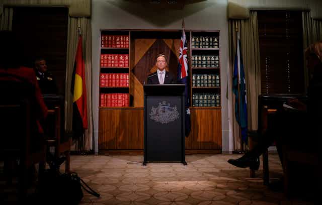 Health Minister Greg Hunt surrounded by the national flags at press conference.