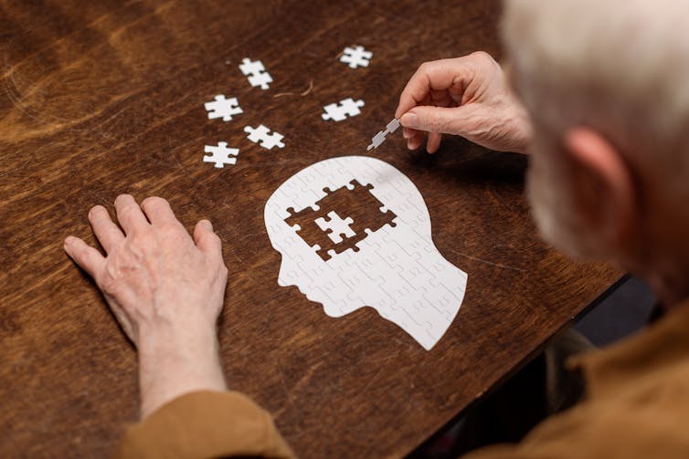 Elderly man filling in the brain of a man in a jigsaw puzzle.