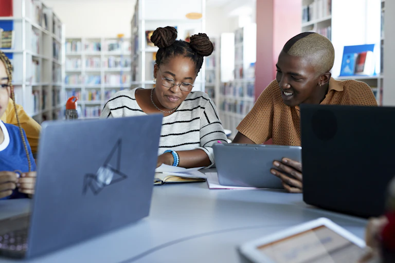 Young students in a library using mobile devices and books.