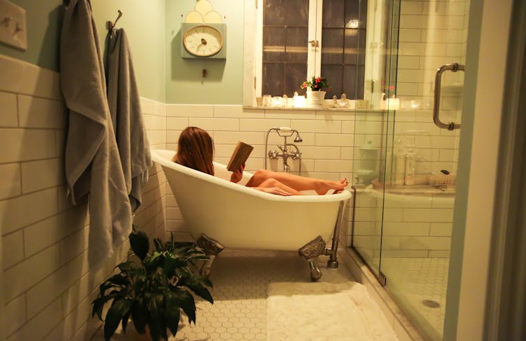 Woman reads in home bathtub.
