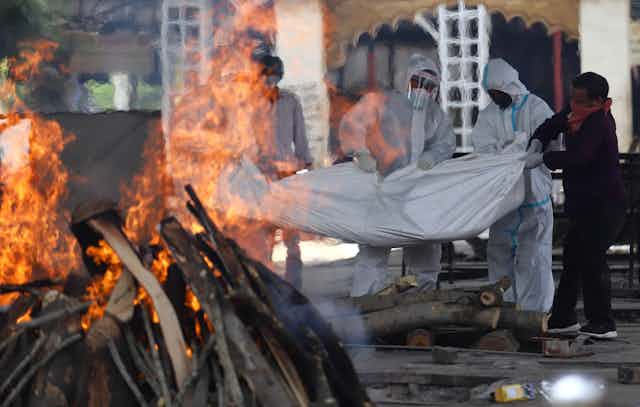 People in face masks carrying a body in a bodybag to a funeral pyre.