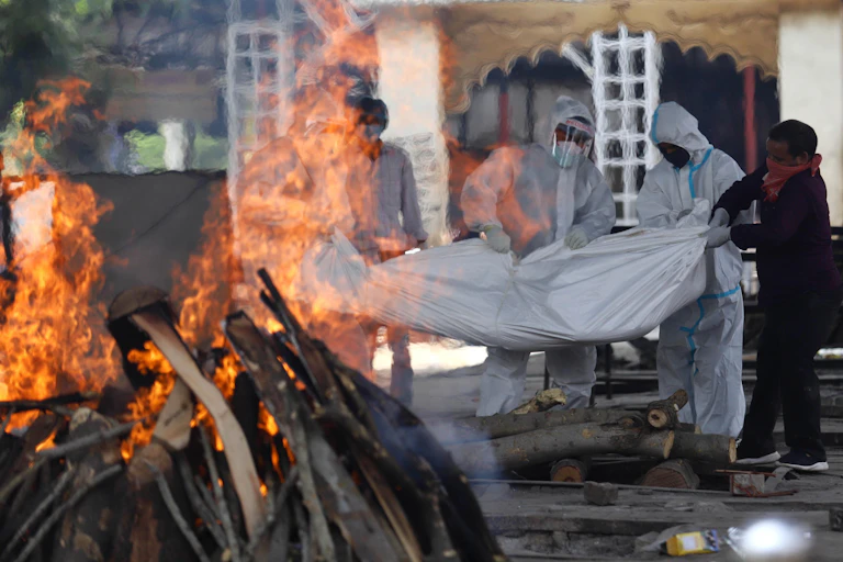 People in face masks carrying a body in a bodybag to a funeral pyre.