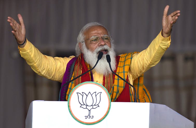Narendra Modi raises his arms in the air and speaks into microphones at a lectern.