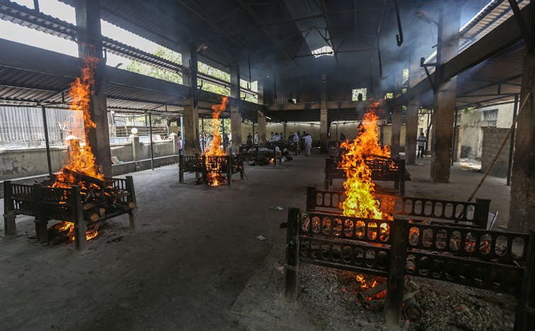Piles of logs burn on small platforms positioned around a large, semi-open hall.