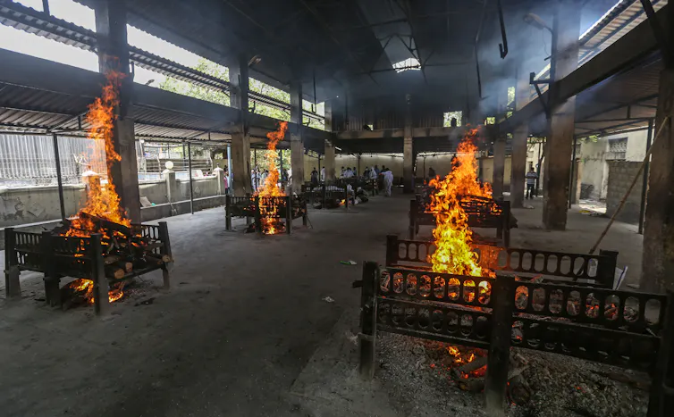 Piles of logs burn on small platforms positioned around a large, semi-open hall.