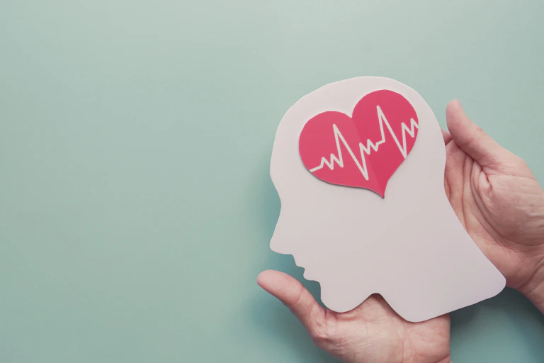 Person holds a paper cutout of a human head, with a heart in the centre representing the brain.