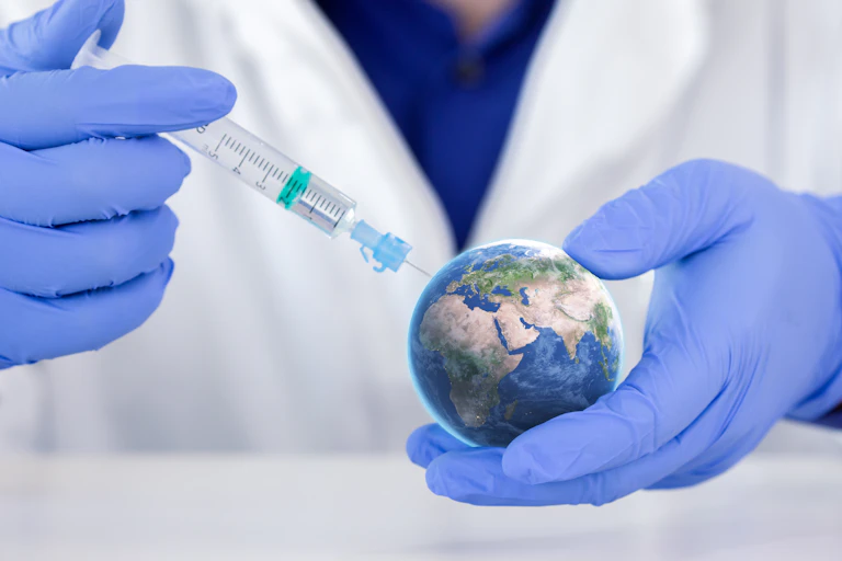 Un sanitario con guantes azules y bata blanca aplicando una inyección a una pequeña bola del mundo.