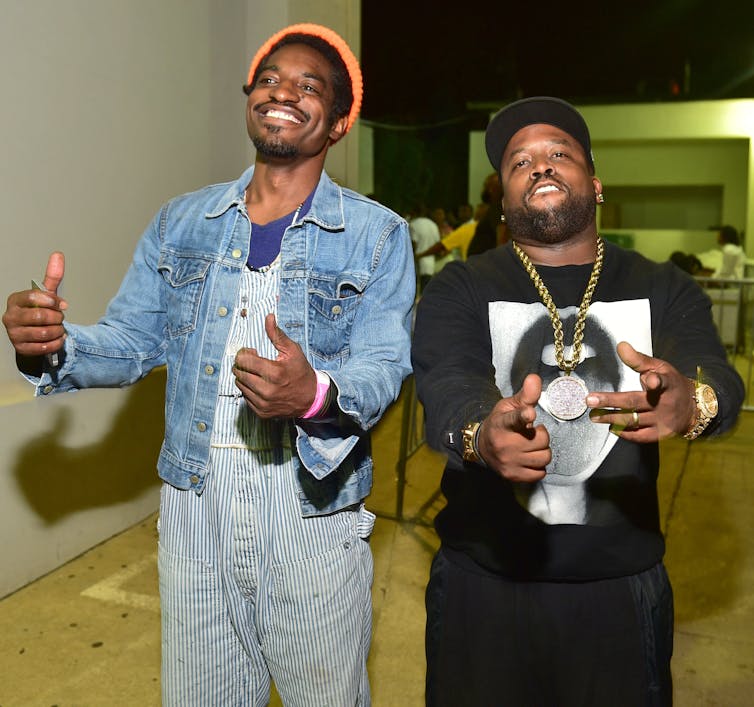 Dois rappers posam para uma foto em um corredor.