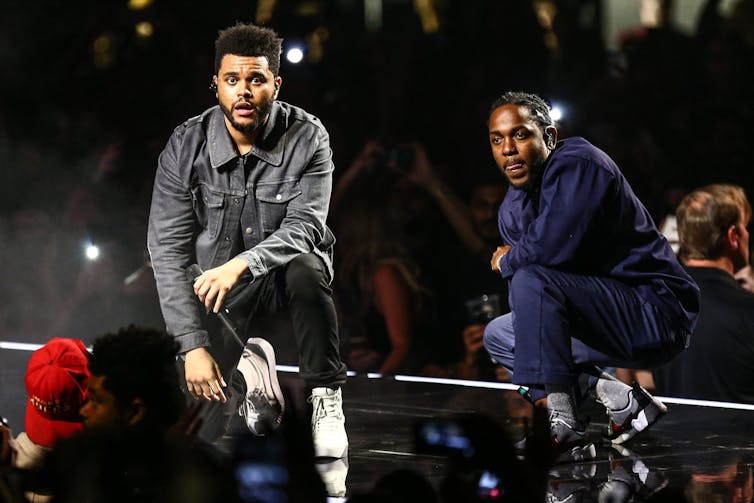 Two rappers kneel on stage.