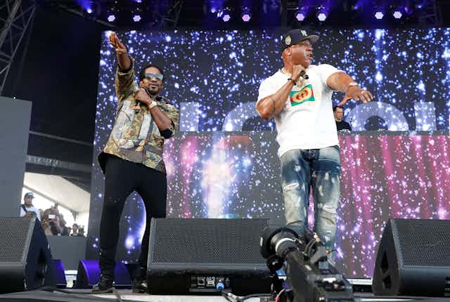 Two rappers perform on stage behind a sparkly background.