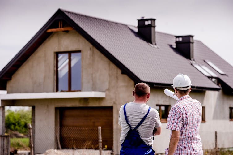 Two men stand in front of a residential construction site.