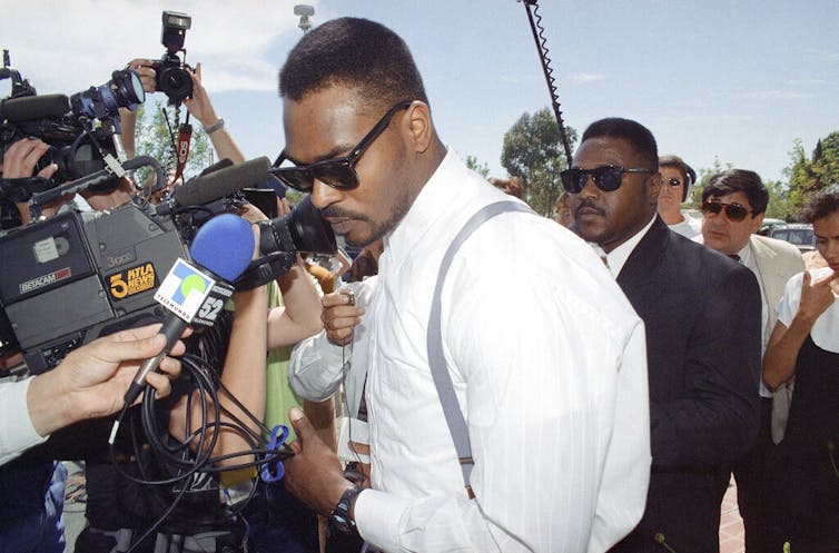 Rodney King squeezes past a crush of reporters and photographers