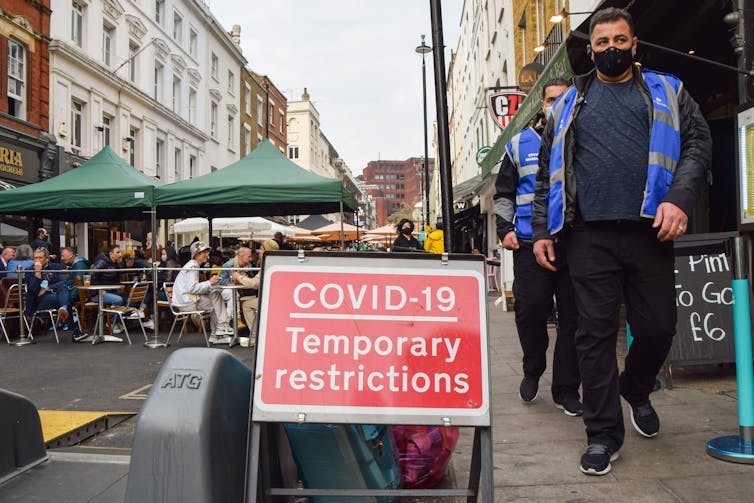 People walk past a COVID restrictions sign on a city street
