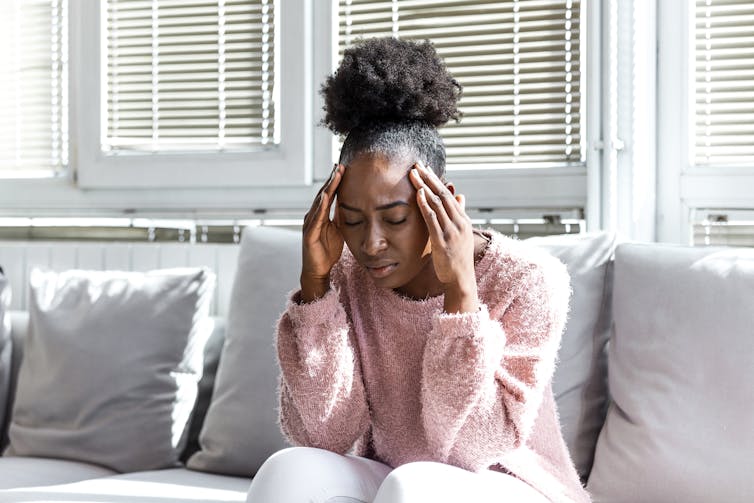 A woman sits on a couch, appearing to have a headache.