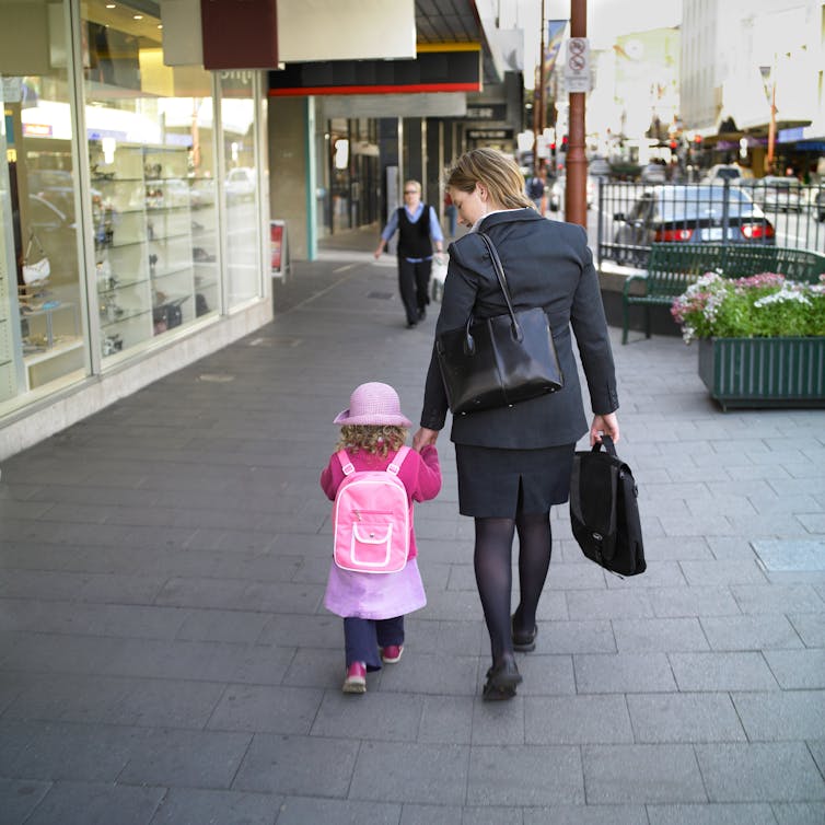 Women in professional wear carrying a briefcase as she takes a young girl to childcare