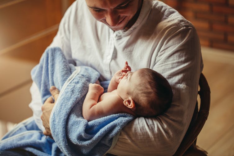 Father cradles young baby wrapped in towel in his arms