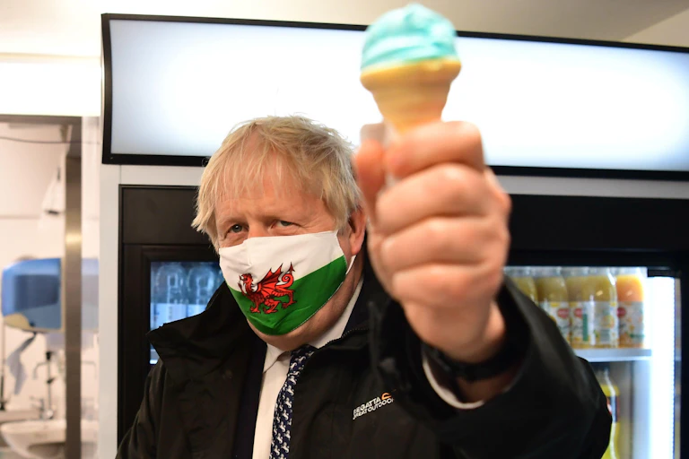 Boris Johnson holds up a blue ice cream while wearing a Welsh flag face mask.