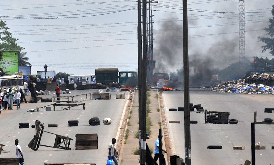 Residents walk past barricades and burning tires on the main road leading to the Abobo district of Abidjan on March 15, 2011 one day after violent fighting between troops loyal to Ivory Coast strongman Laurent Gbagbo and forces backing internationally recognized President Alassane Ouattara