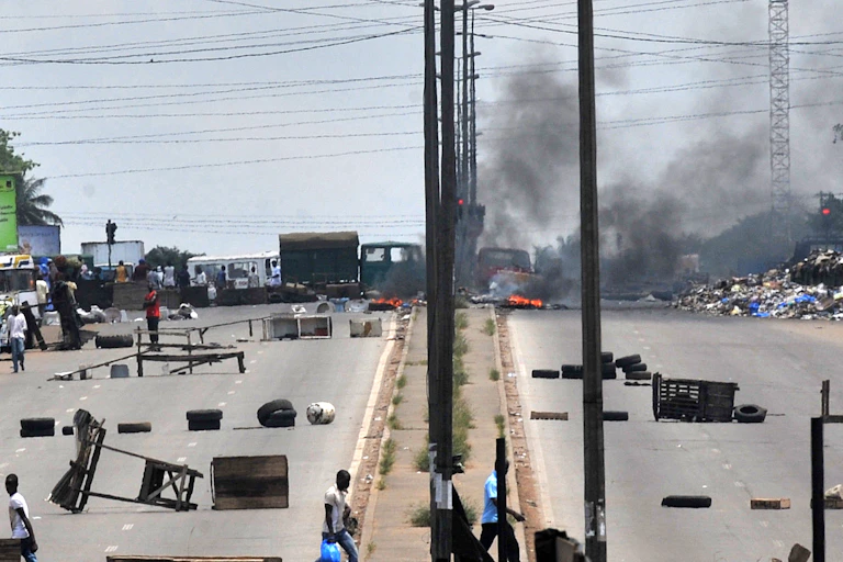Residents walk past barricades and burning tires on the main road leading to the Abobo district of Abidjan on March 15, 2011 one day after violent fighting between troops loyal to Ivory Coast strongman Laurent Gbagbo and forces backing internationally recognized President Alassane Ouattara