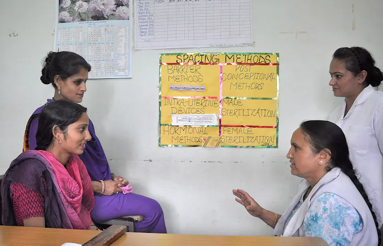 Women sit talking to one another in front of a poster depicting contraceptive methods.