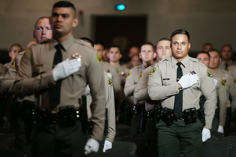 Young police officers in uniform stand with hands over their hearts; all are male