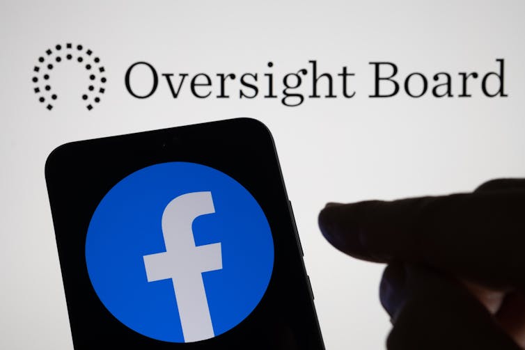 The oversight board's logo behind a phone screen with the Facebook icon