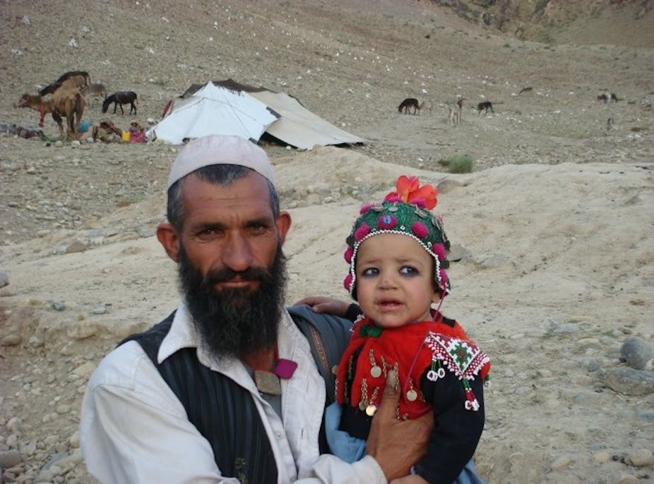 A man and a child in front of a tent with livestock behind