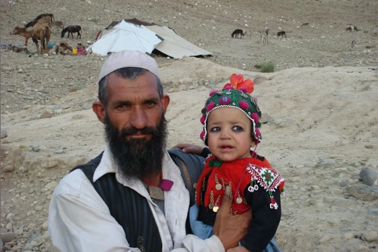 A man and a child in front of a tent with livestock behind