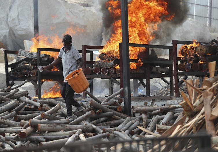 A worker sprinkles fuel on burning funeral pyres