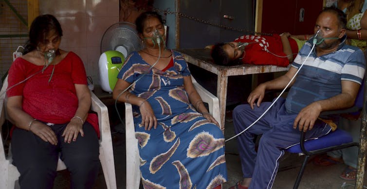 Four people receive oxygen, three sitting in chairs and another lying on a table.