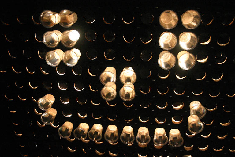 A black pegboard with clear plastic pegs marking out a smiley face and white light from behind the pegboard