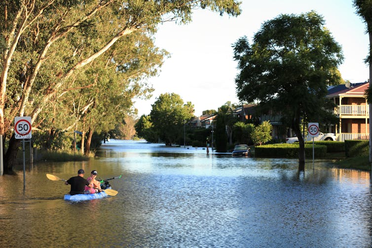 A man and woman use a kayak to travel up a flooded street.