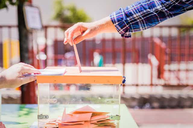 Una mano de hombre deposita un sobre en una urna instalada en el exterior de un colegio electoral en Madrid.