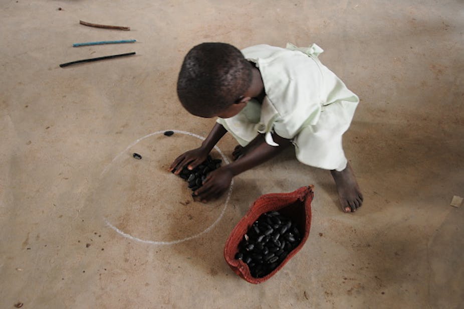 A child playing with baobab seed pods on the ground.