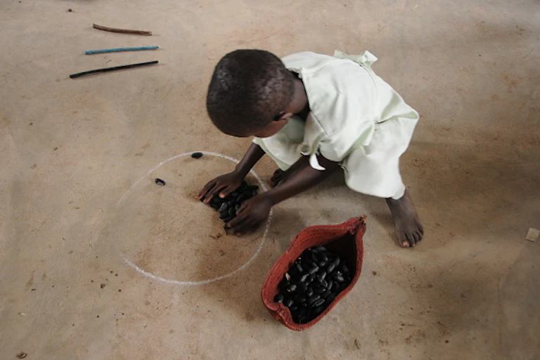 A child playing with baobab seed pods on the ground.