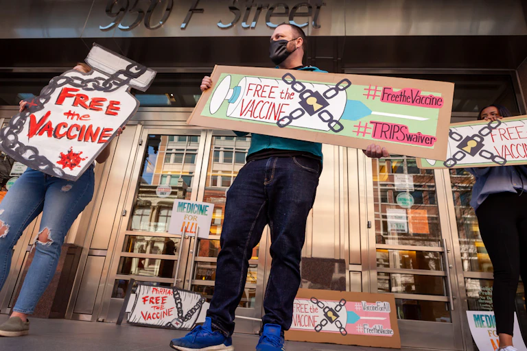Two protesters hold signs demanding the US waives vaccine patents.