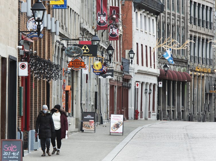 Two people wearing masks walk along a street.