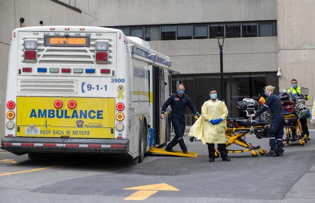 Paramedics wheeling gurneys to an ambulance bus in a parking lot