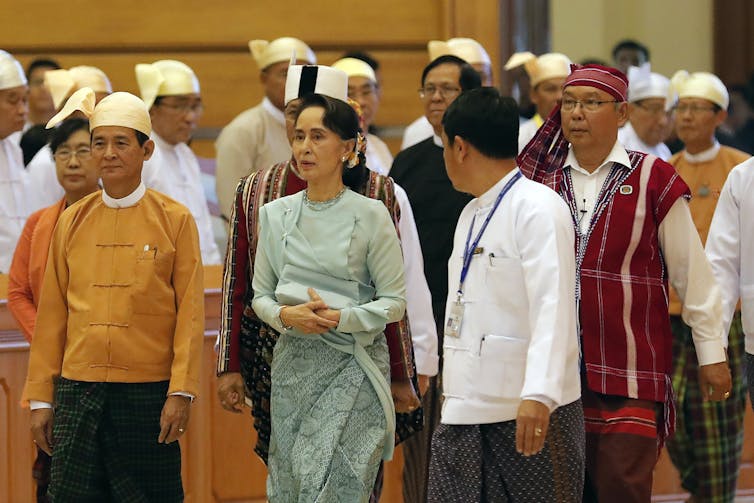 Aung San Suu Kyi, in a green dress, walks alongside many men