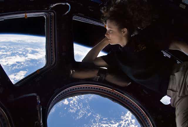 A woman in a windowed room looking at the earth from space. 