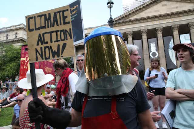Protester in a mask holding up a sign that says 'climate action now'
