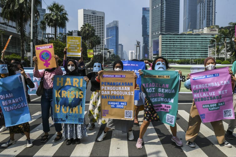 Lima orang aktivis lingkungan membawa spanduk berwarna-warni berdiri di trotoar.