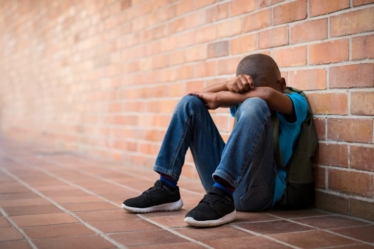 School kid with his head in his hands sitting on the ground.