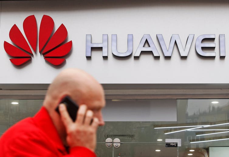 A man on the phone walking in front of a Huawei store