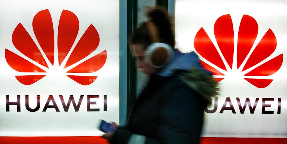A woman on her phone walking by Huawei signs