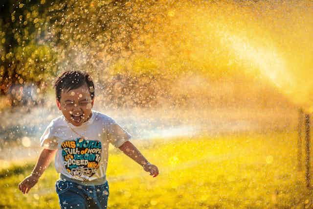A little boy runs through a sprinkler in bright golden sunshine
